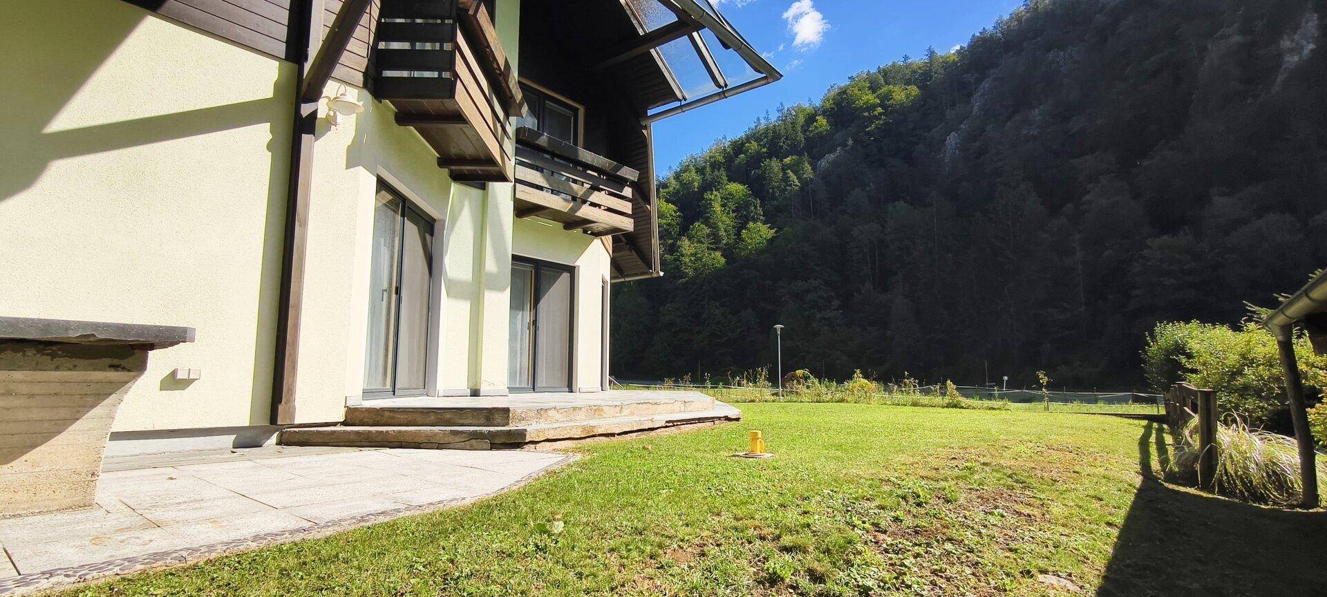 Seitenansicht des Hauses mit großer Rasenfläche und Zugang zur Terrasse.