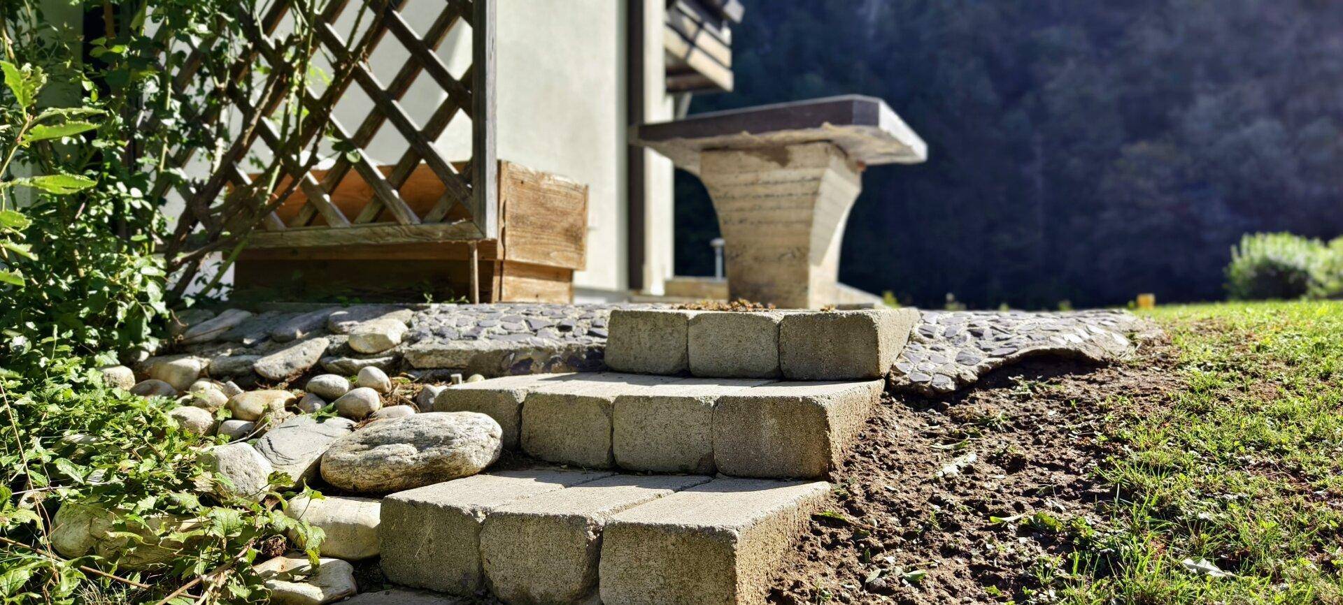 Rustikale Steinstufen führen zu einem erhöhten Bereich im Garten mit Sitzgelegenheit.