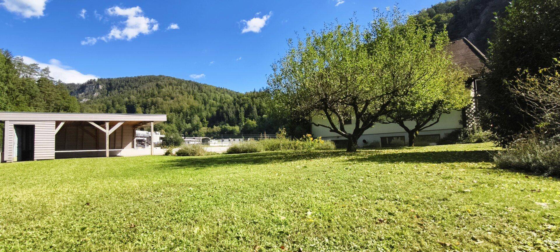 Weitläufige Rasenfläche mit Carport und Panoramablick auf die umliegende Berglandschaft.