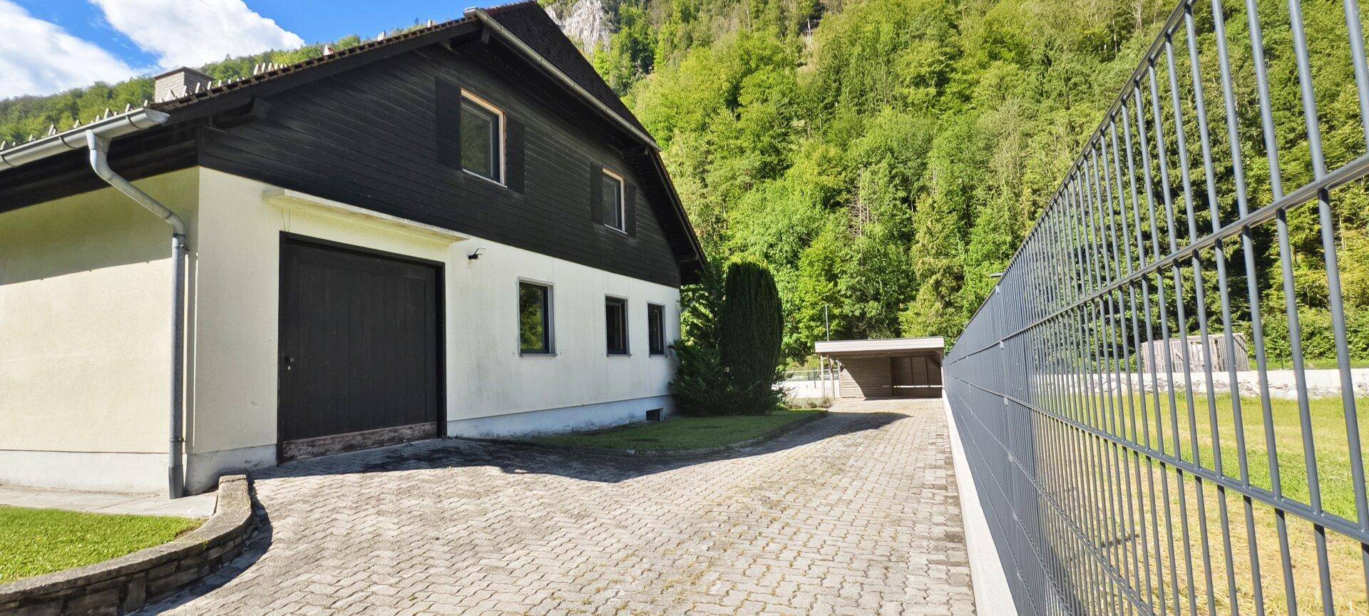 Seitenansicht des Hauses mit Garage, gepflasterter Auffahrt und Zaun.