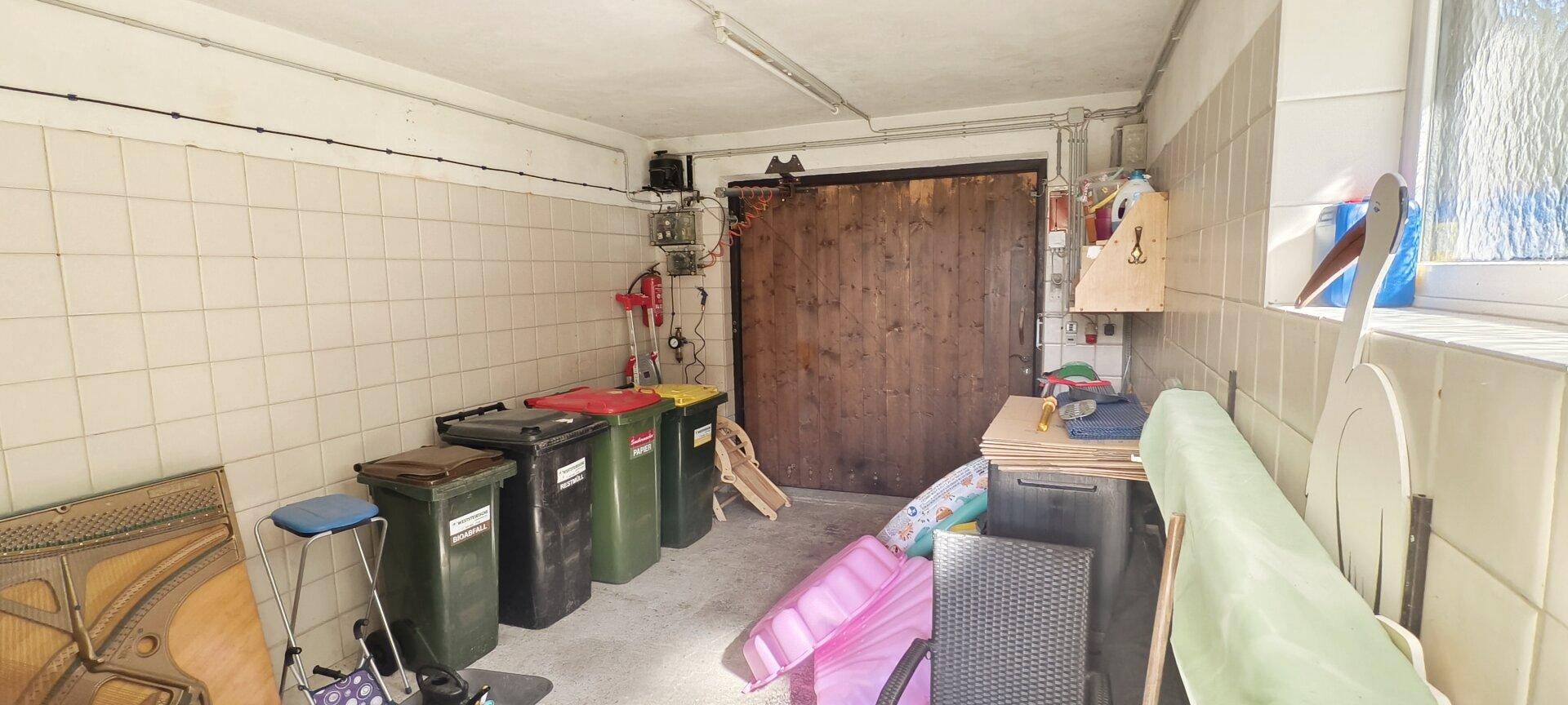 Geräumige Garage oder Abstellraum mit Fliesenwänden und Platz für diverse Gegenstände.