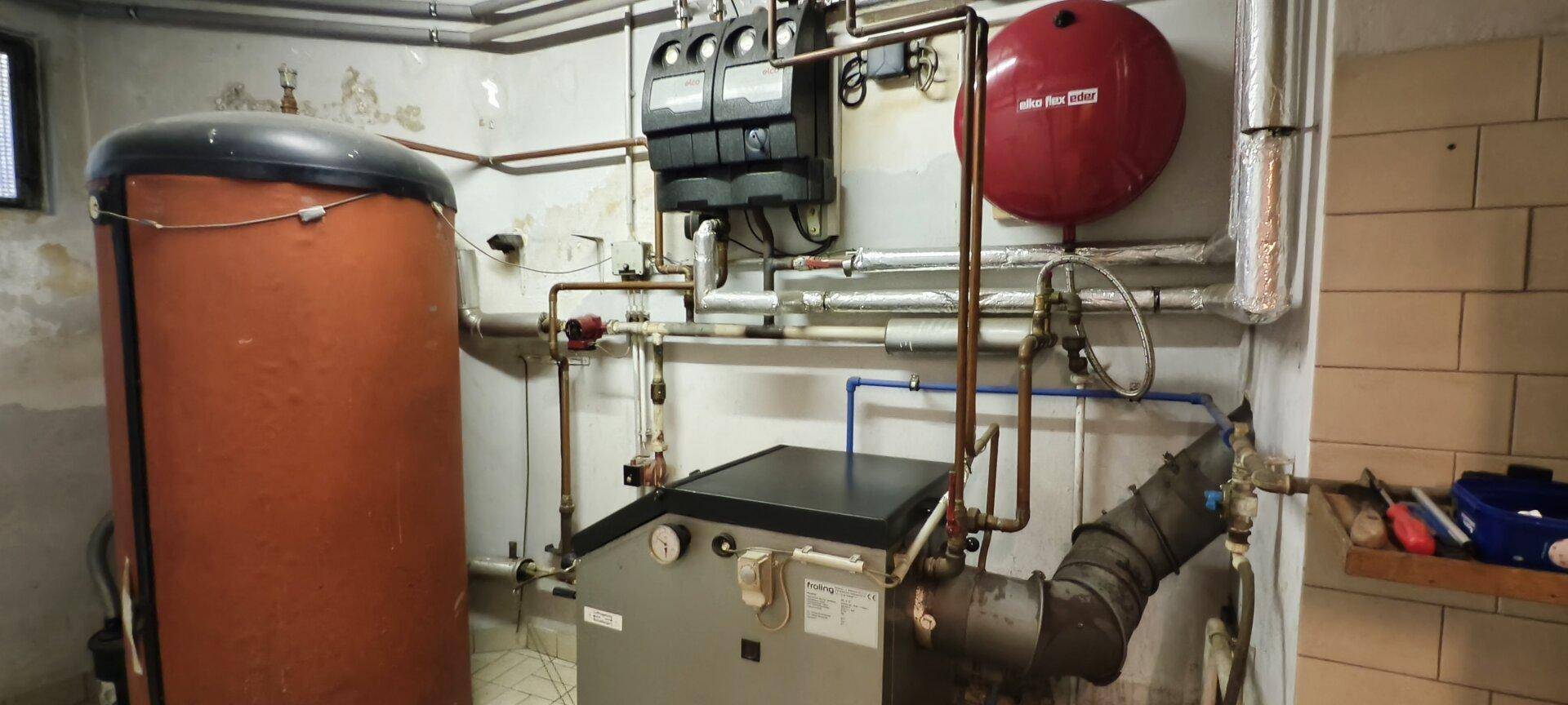 Heizungsraum mit Warmwasserspeicher und komplexen Rohrleitungen für die Gebäudetechnik.