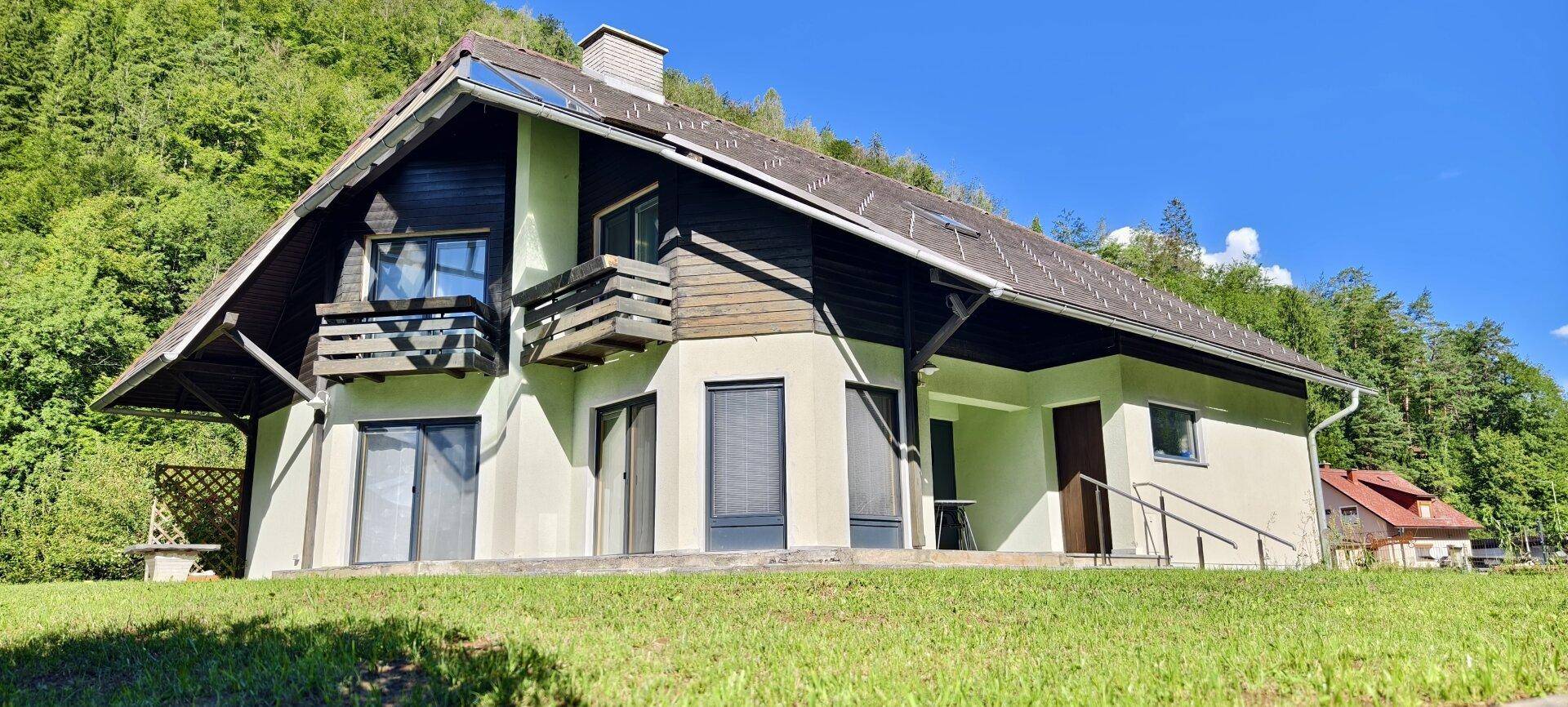 Attraktives Haus mit Balkon und großen Fenstern, umgeben von üppiger Natur.