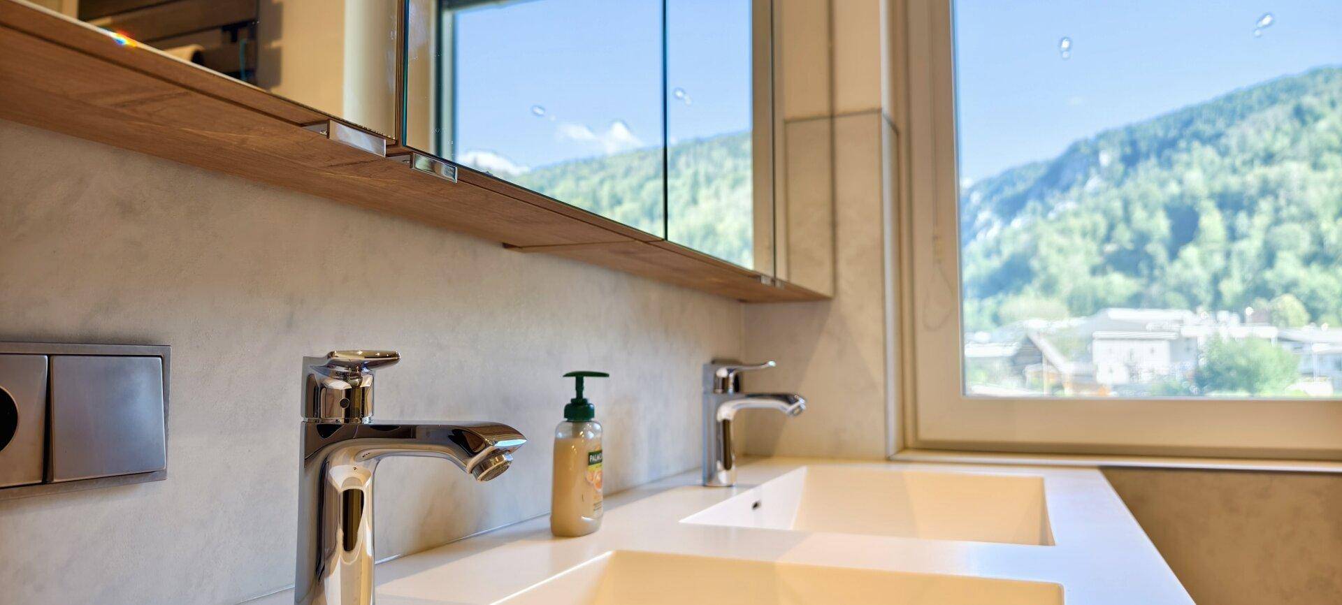 Modernes Badezimmer mit Doppelwaschbecken, großem Spiegel und Bergblick durch das Fenster.