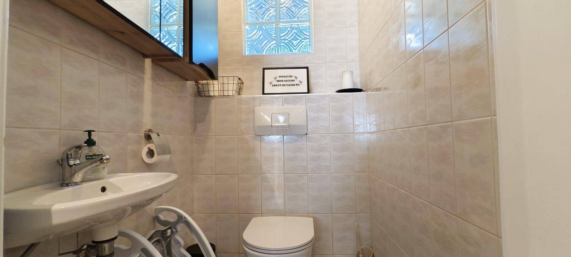 Kleines Gäste-WC mit Wand-WC, Waschbecken und Fliesen an den Wänden.