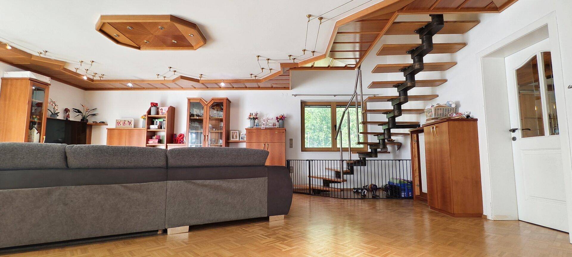 Geräumiges Wohnzimmer mit Holztreppe, Parkettboden und Holzdeckenverkleidung.