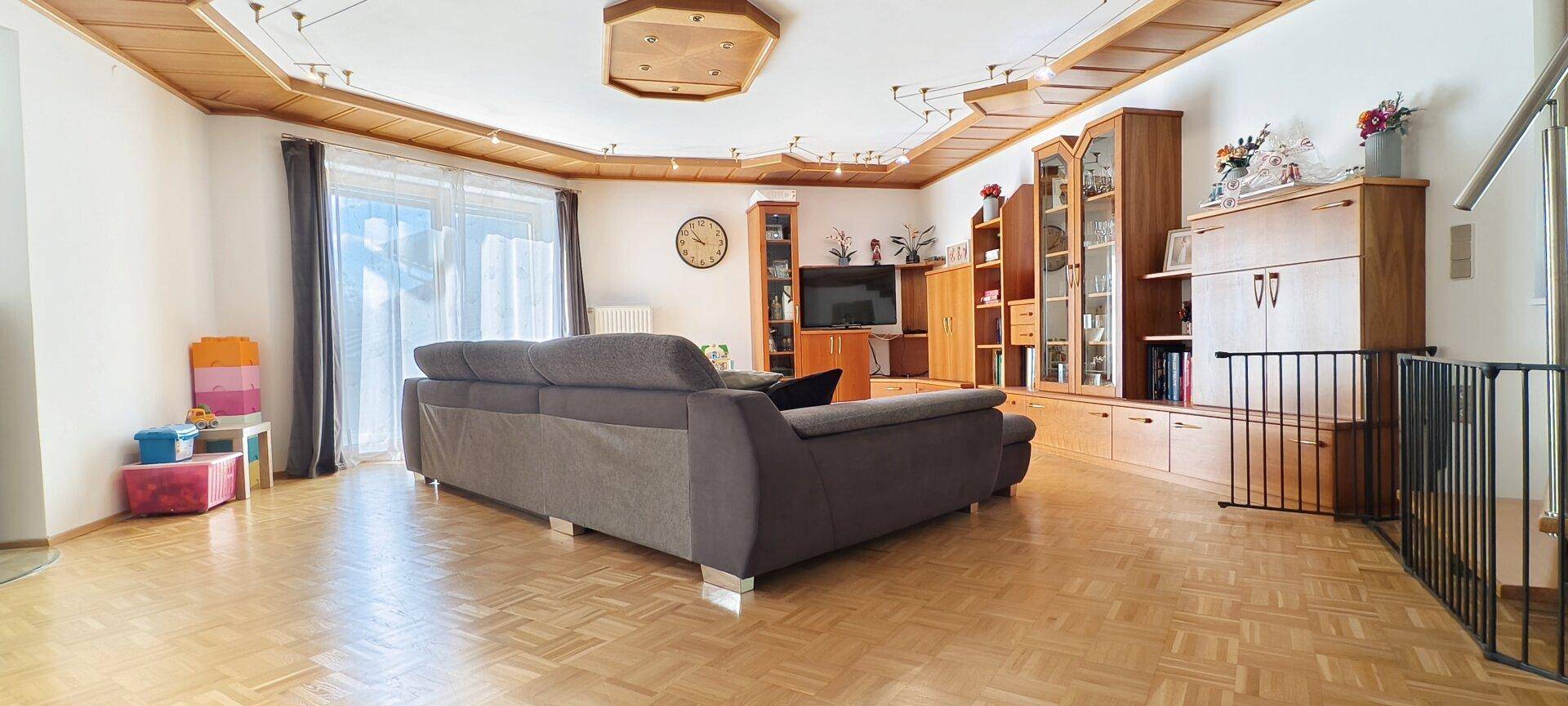 Großzügiges Wohnzimmer mit bequemer Couch, Parkettboden und viel Tageslicht.