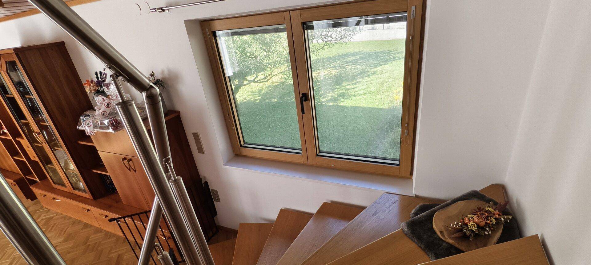 Holztreppe mit Fenster, das einen Blick auf die grüne Umgebung bietet.