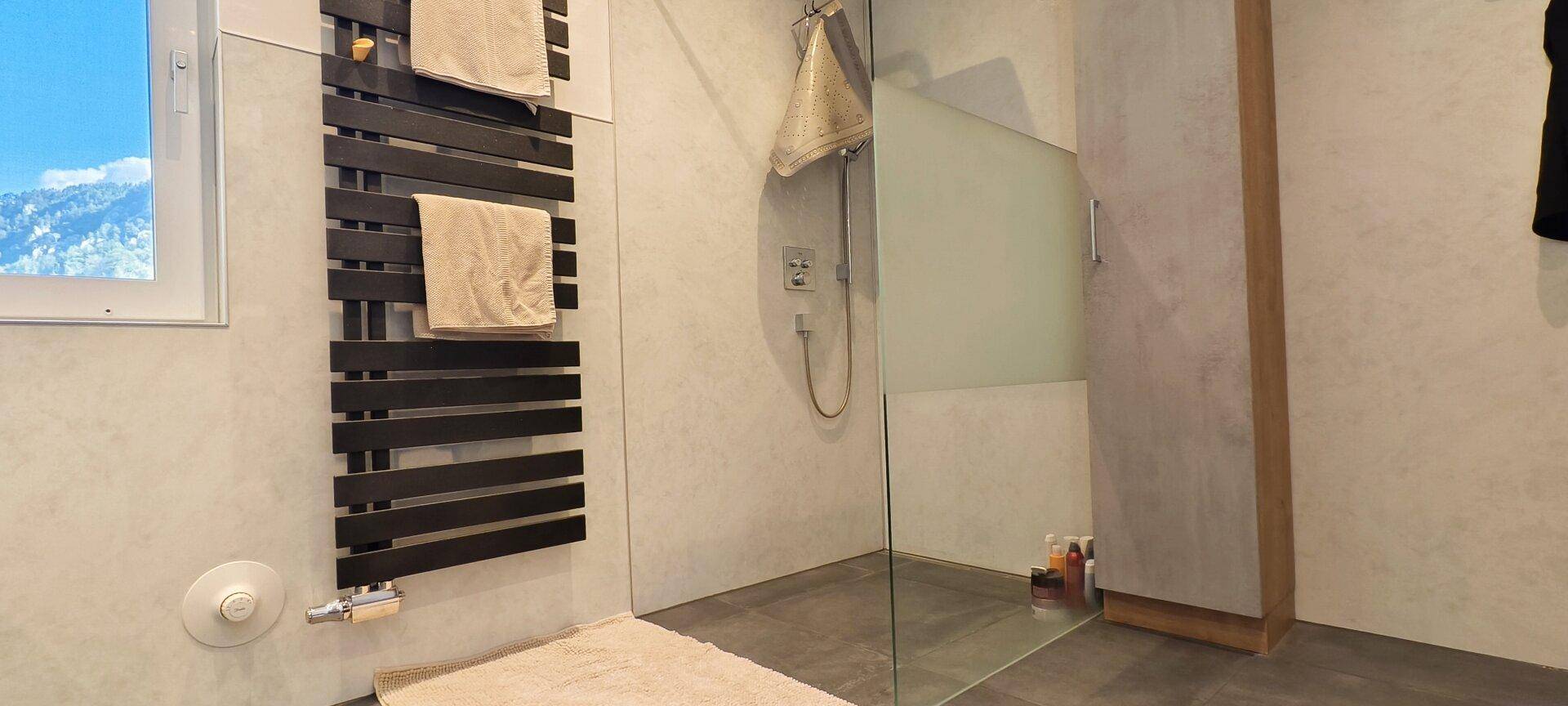 Modernes Badezimmer mit ebenerdiger Dusche, Glasabtrennung und beheiztem Handtuchhalter.