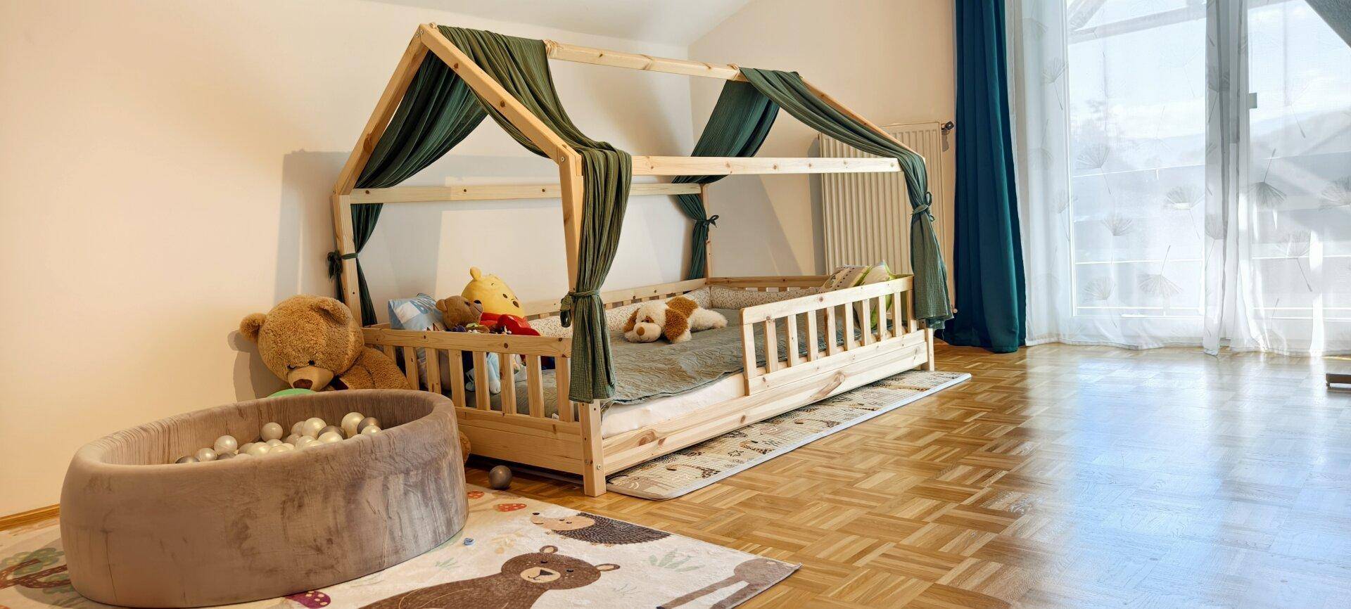 Helles Kinderzimmer mit einzigartigem Hausbett und Zugang zu einem Balkon oder einer Terrasse.