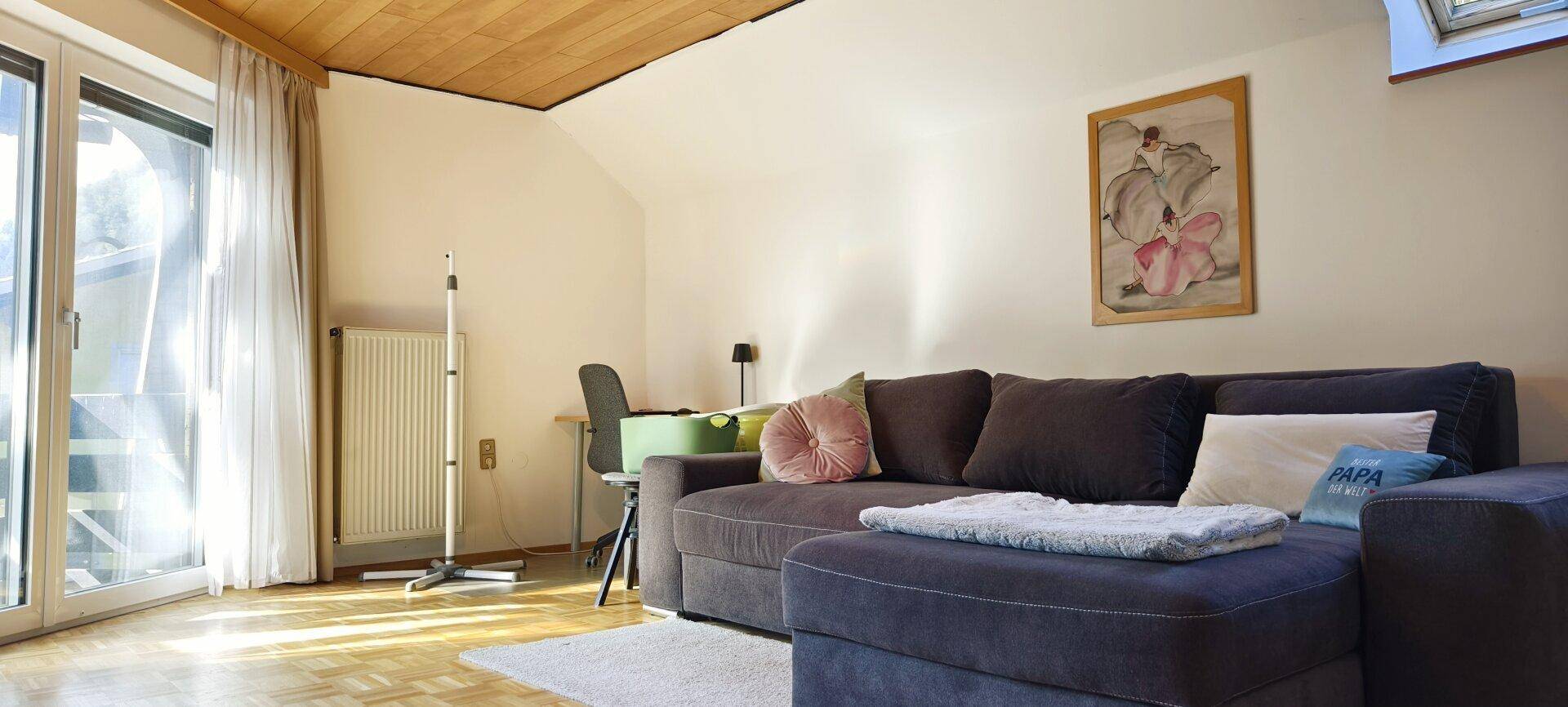 Gemütlicher Wohnbereich mit Sofa, Schreibtisch und Dachschräge, ergänzt durch ein Dachfenster.