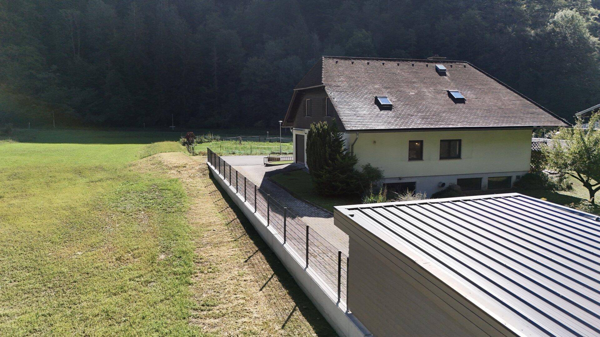 Weitläufiges Grundstück mit Einfamilienhaus, großer Rasenfläche und angrenzendem Waldgebiet.