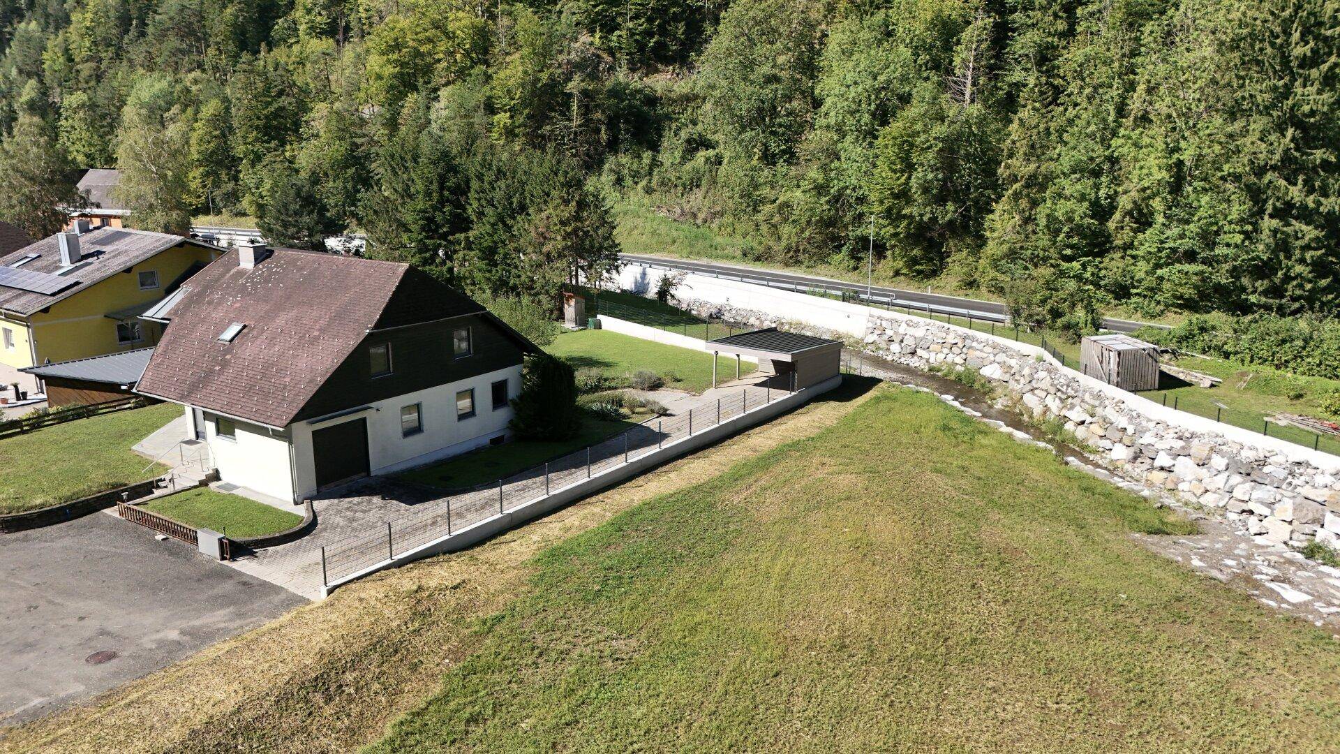 Haus in ländlicher Umgebung mit Nebengebäude, umgeben von Wald und Wiesen.