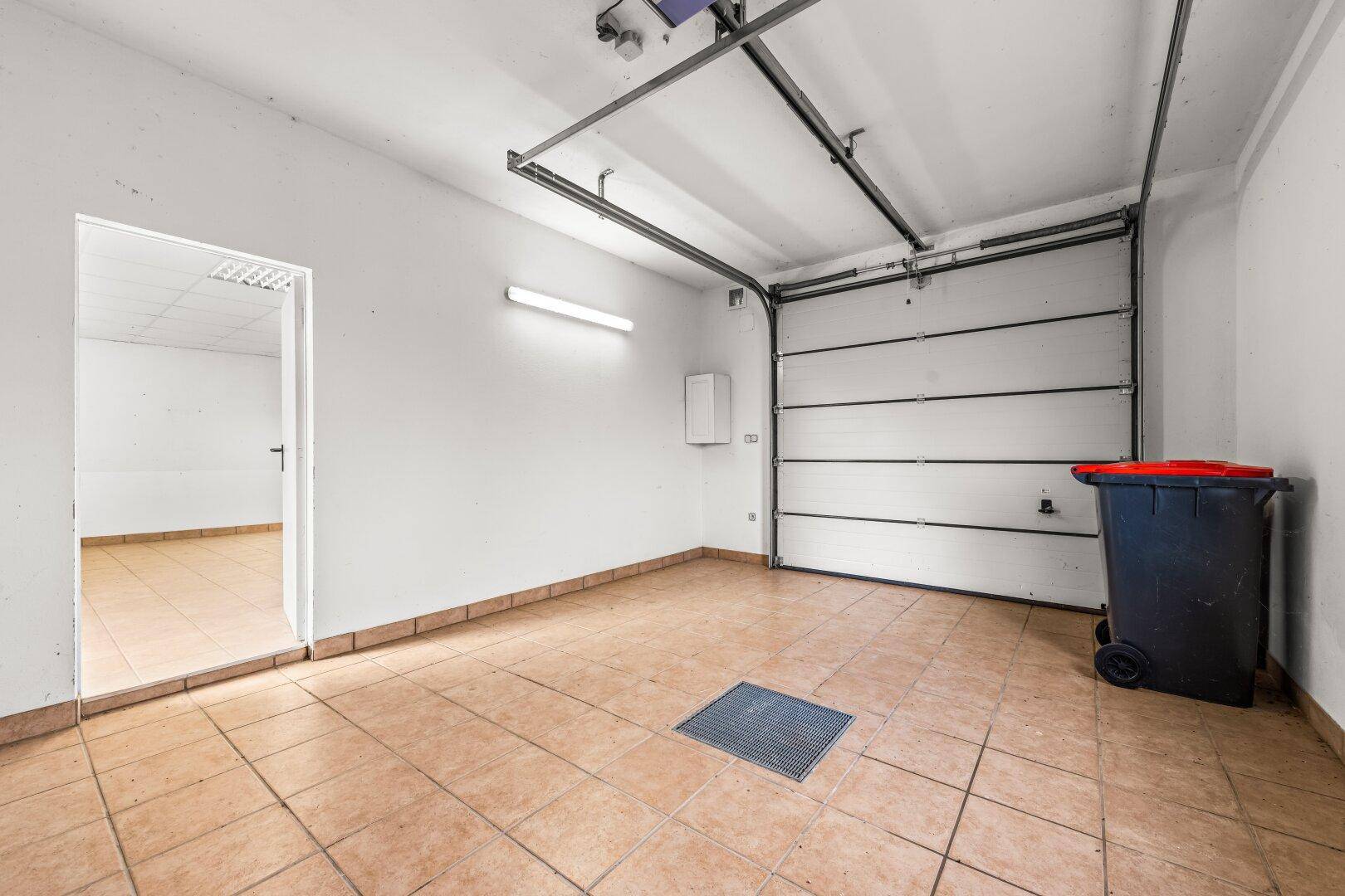 Geräumige Garage mit Fliesenboden, weiß gestrichenen Wänden und einem Rolltor.