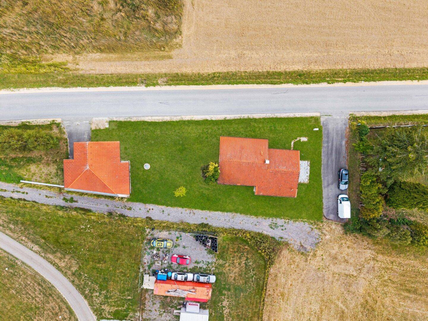 Draufsicht auf zwei Gebäude mit roten Ziegeldächern, umgeben von Grünflächen und Feldern.