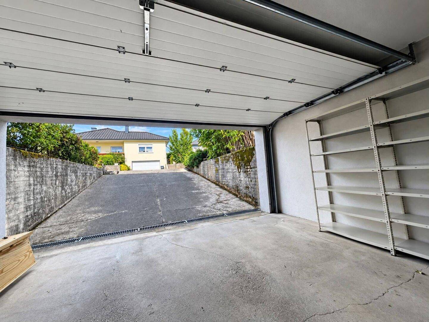Geräumige Garage mit Regalen und Blick auf die Einfahrt und das Nachbarhaus.