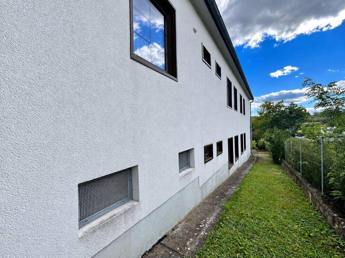 Schlichte Seitenfassade des Hauses mit kleinen Fenstern und angrenzendem Rasenstreifen.