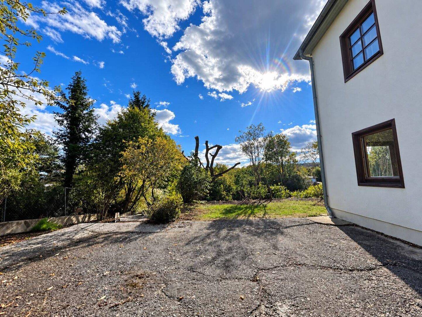 Außenansicht des Hauses mit Einfahrt und Gartenbereich unter blauem Himmel.