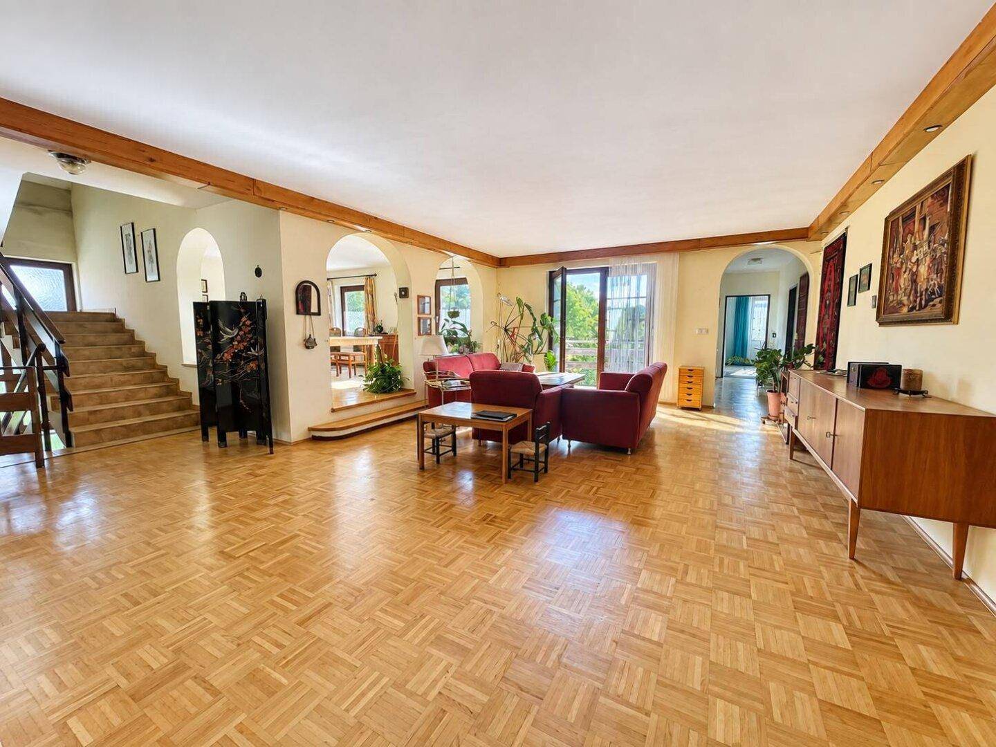 Geräumiges Wohnzimmer mit Fischgrätparkett, Holzbalken und Zugang zur Terrasse.