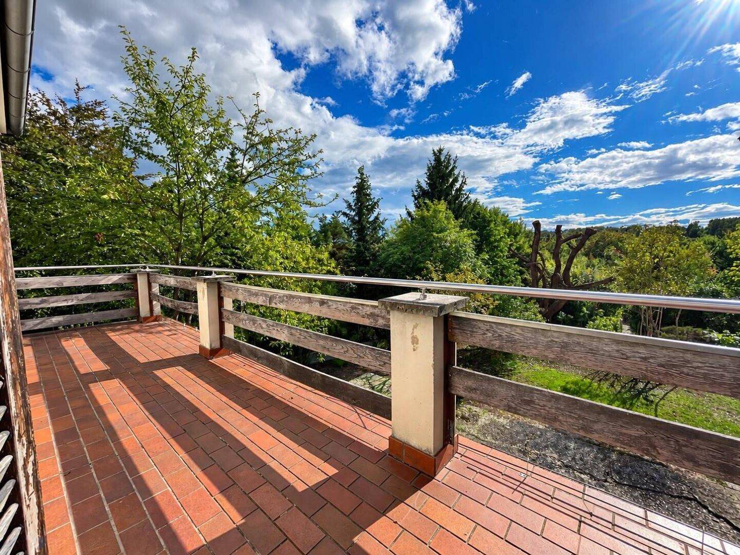 Weitläufige Terrasse mit Holzgeländer und freiem Blick auf die grüne Umgebung.