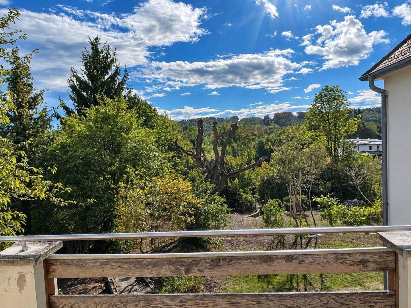 Panoramablick von der Terrasse über die hügelige, bewaldete Landschaft unter blauem Himmel.
