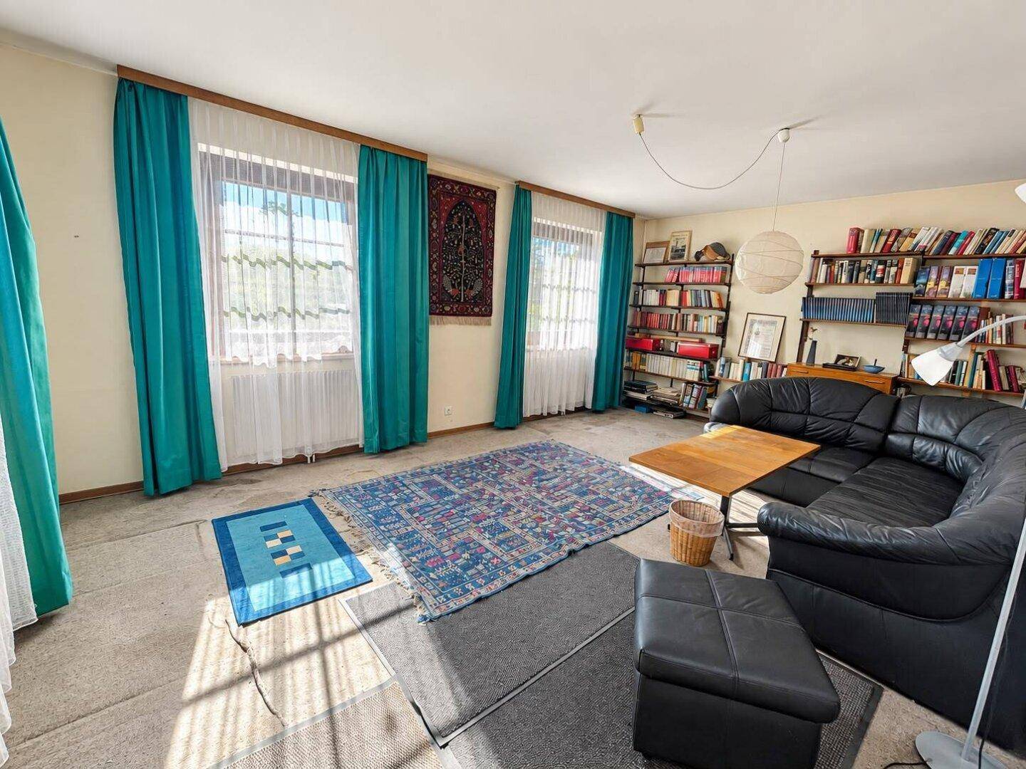 Geräumiges Arbeitszimmer mit Teppichboden, großem Bücherregal und bequemer Couch.