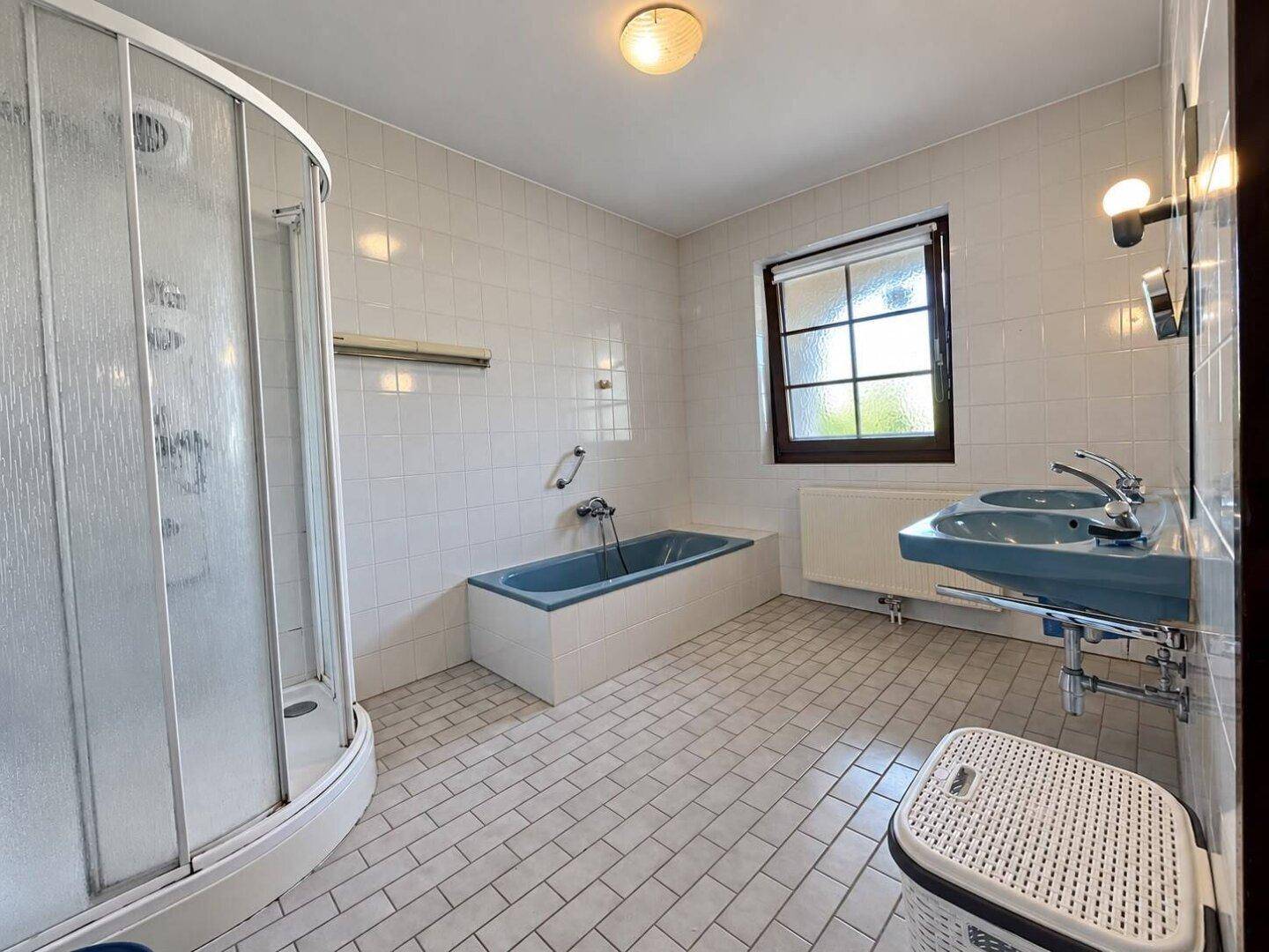 Badezimmer mit blauer Badewanne, Duschkabine und Fenster.