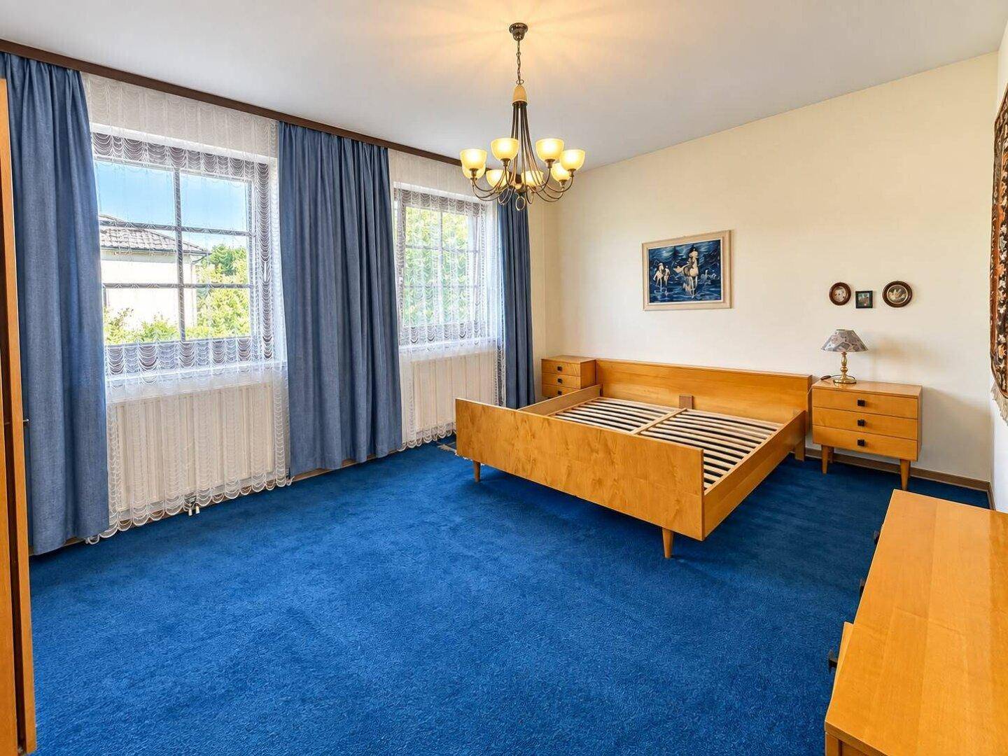 Schlafzimmer mit blauem Teppichboden, Holzmöbeln und klassischem Kronleuchter.