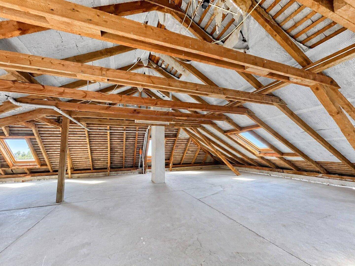 Geräumiger Dachboden mit sichtbaren Holzbalken und Dachfenstern für zukünftigen Ausbau.