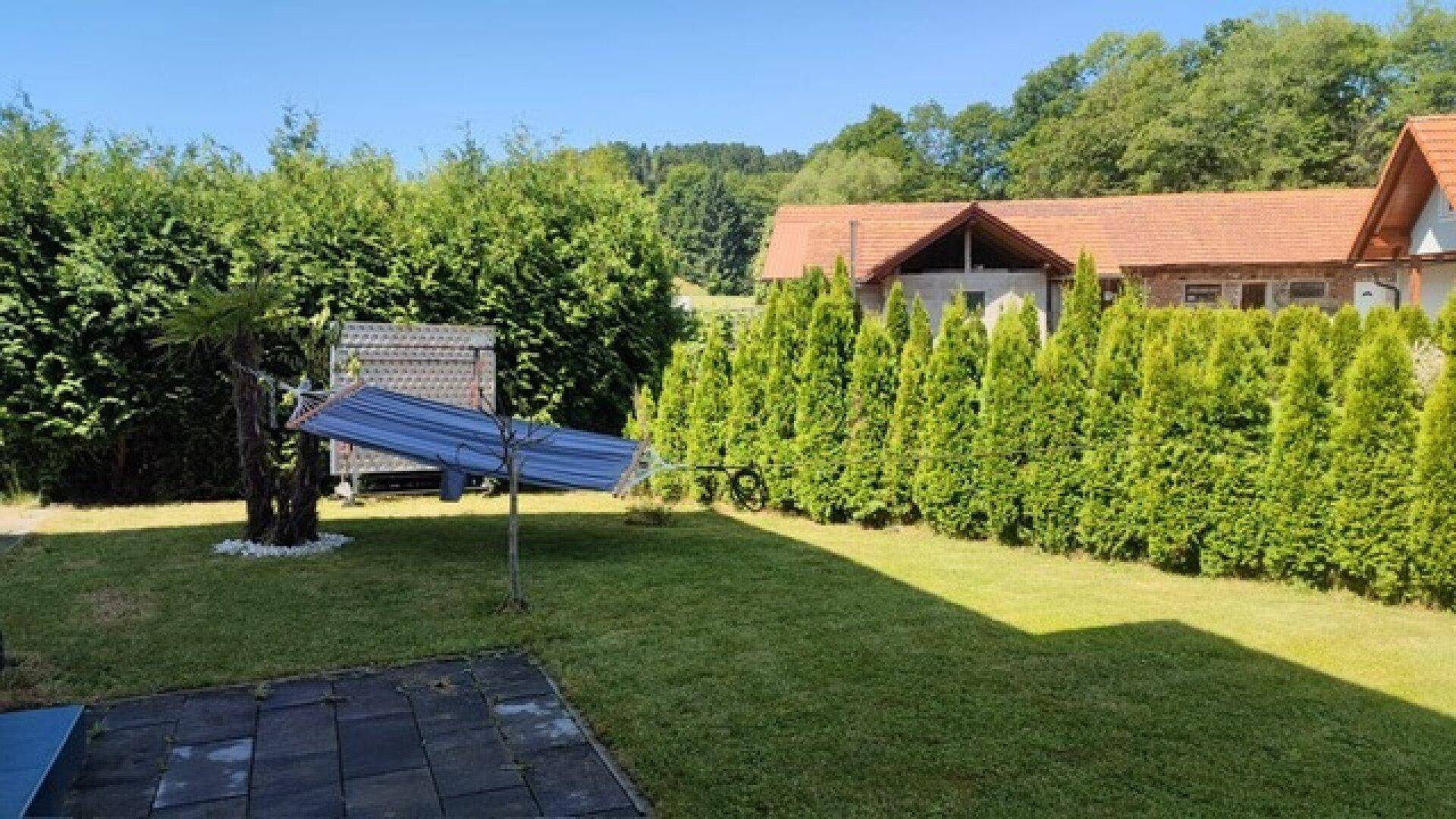 Gepflegter Gartenbereich mit Rasenfläche, hohen Hecken und einem Haus im Hintergrund.