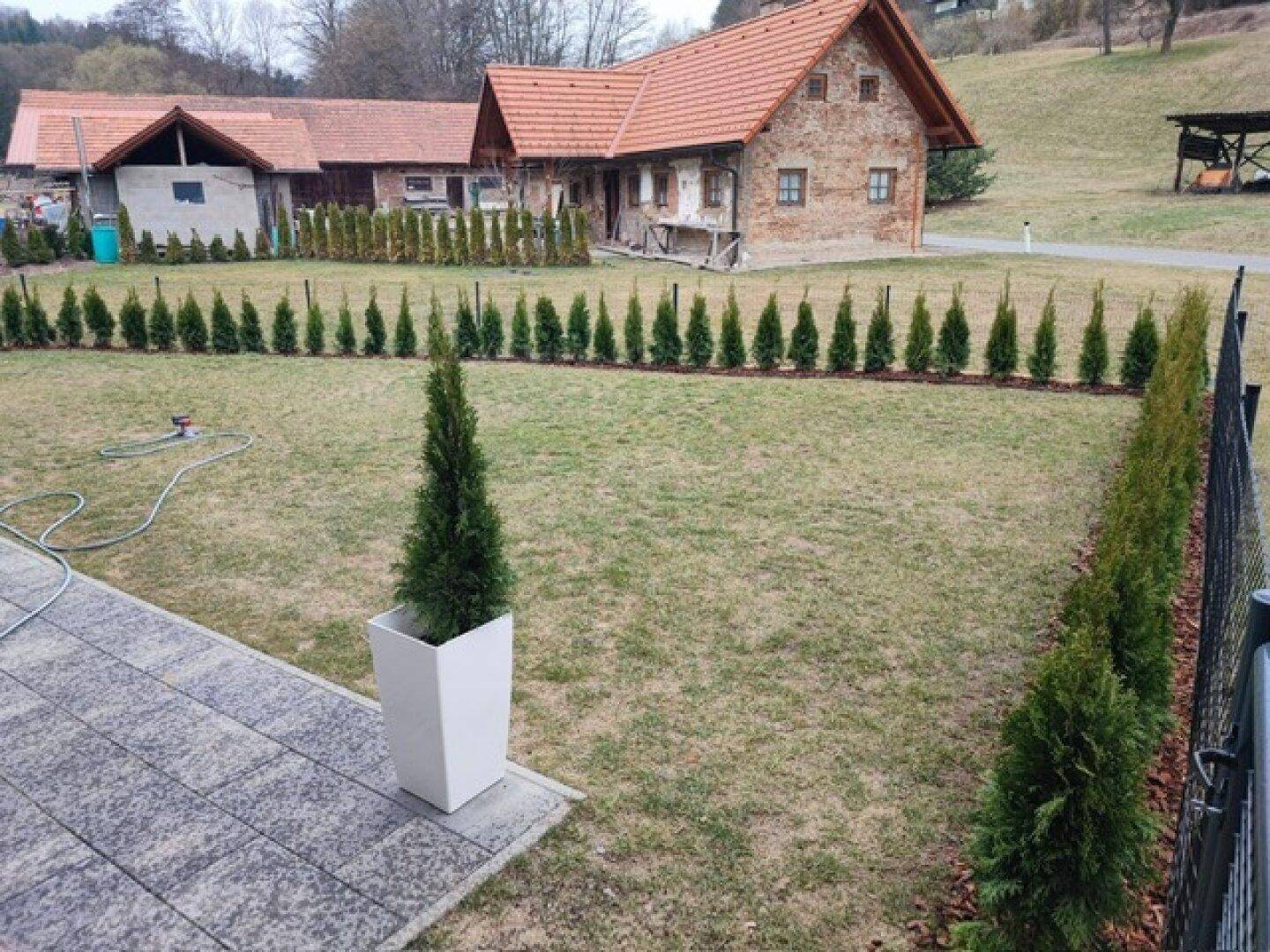 Gartenbereich mit Rasen, gepflastertem Weg und traditionellen Häusern im Hintergrund.