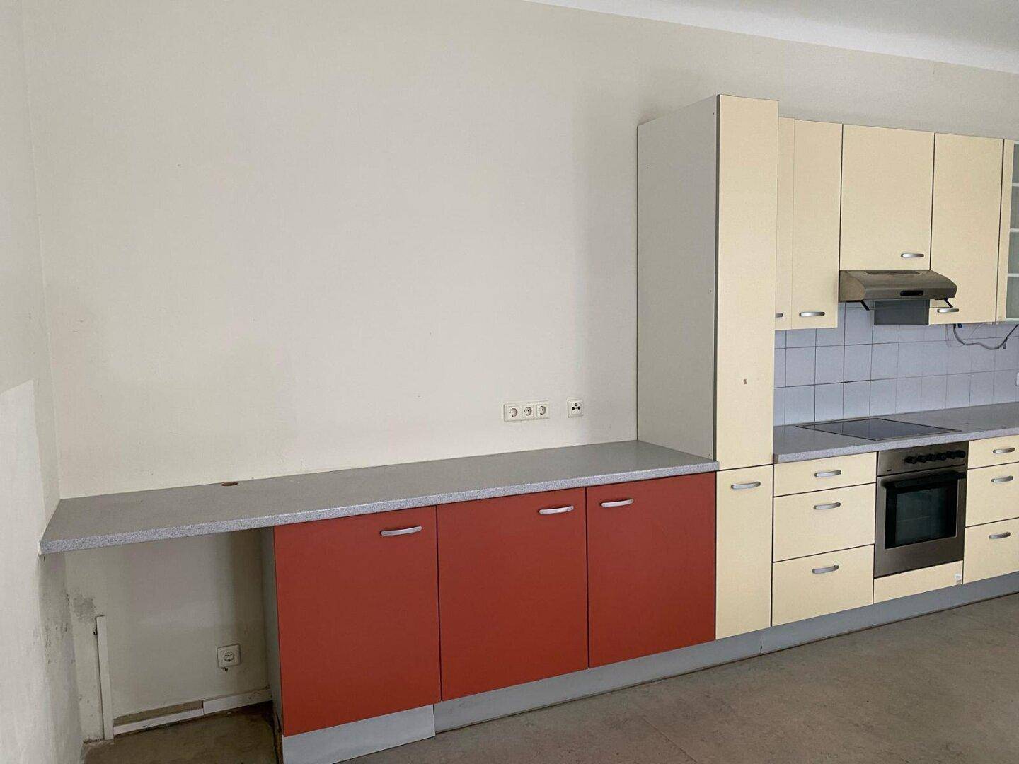 Küchenzeile mit beigen und roten Unterschränken, einer Arbeitsplatte und einer gefliesten Rückwand.