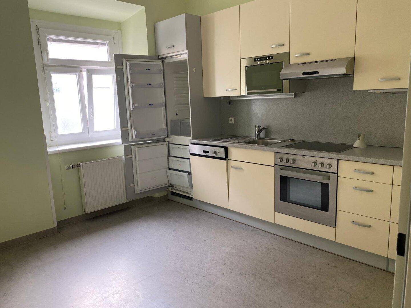 Helle Küche mit beigen Schränken, Einbaugeräten und einem Fenster, das viel Tageslicht hereinlässt.