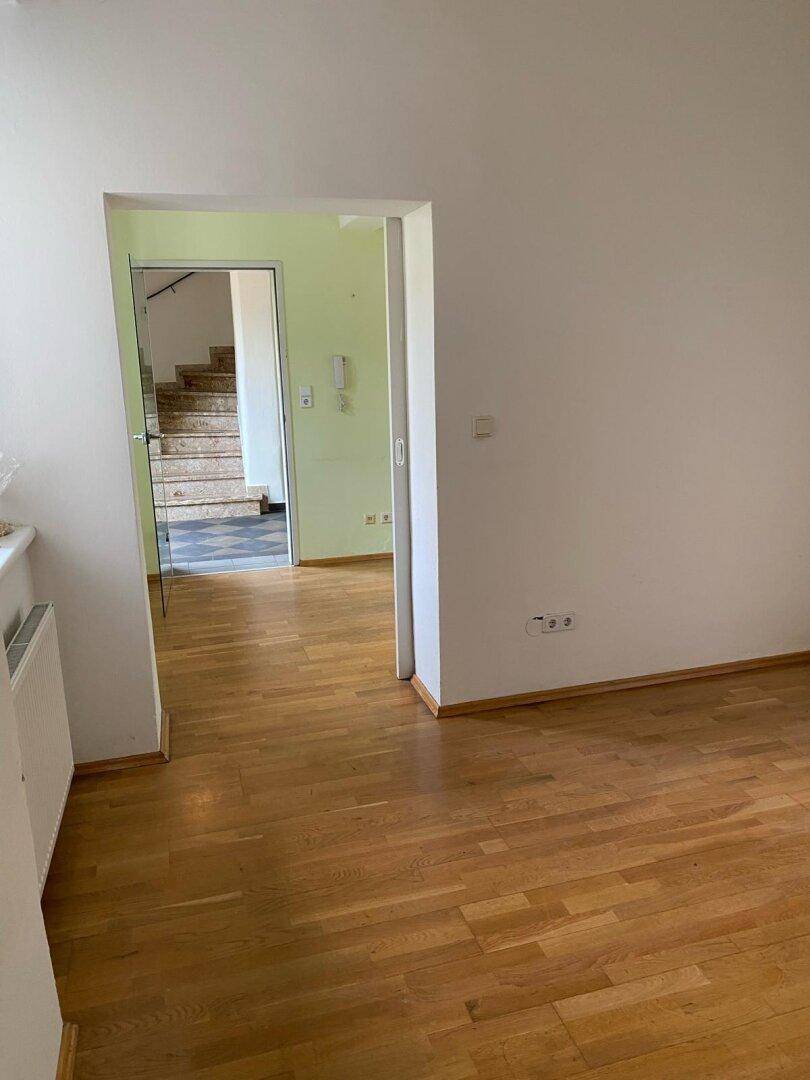 Wohnbereich mit hellem Holzparkettboden und Blick auf eine Treppe in einem angrenzenden Raum.