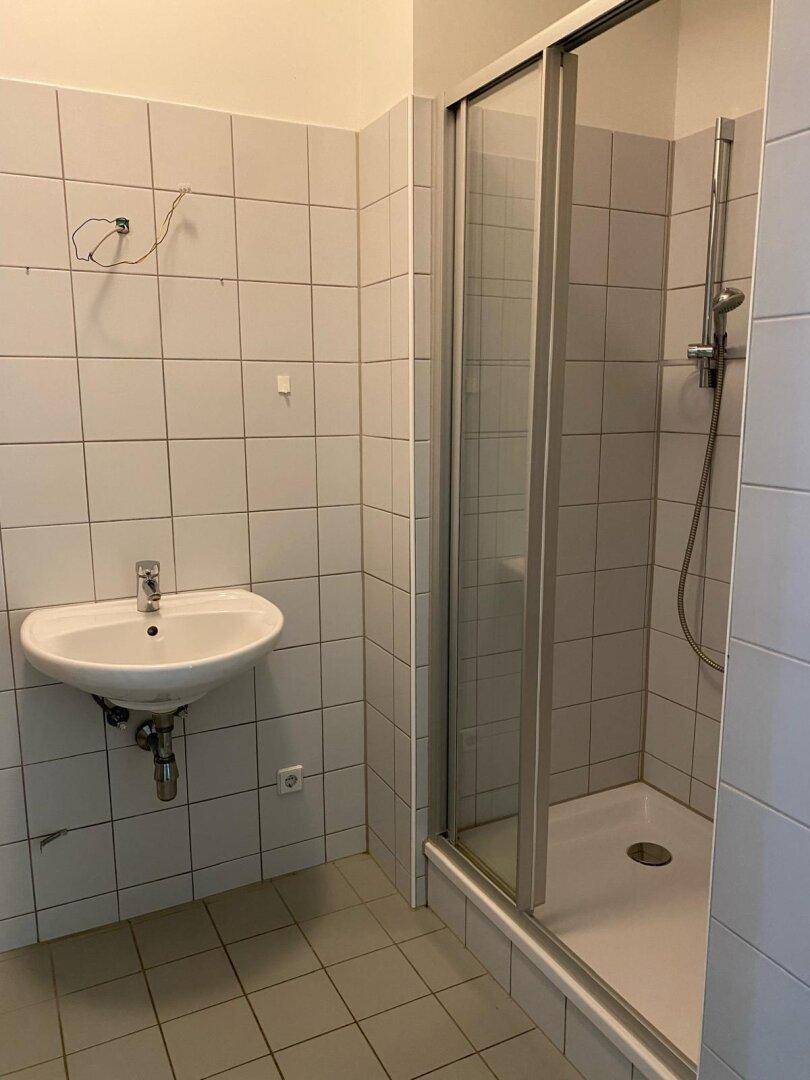 Badezimmer mit weißen Fliesen, einem Waschbecken und einer Duschkabine mit Glasschiebetür.