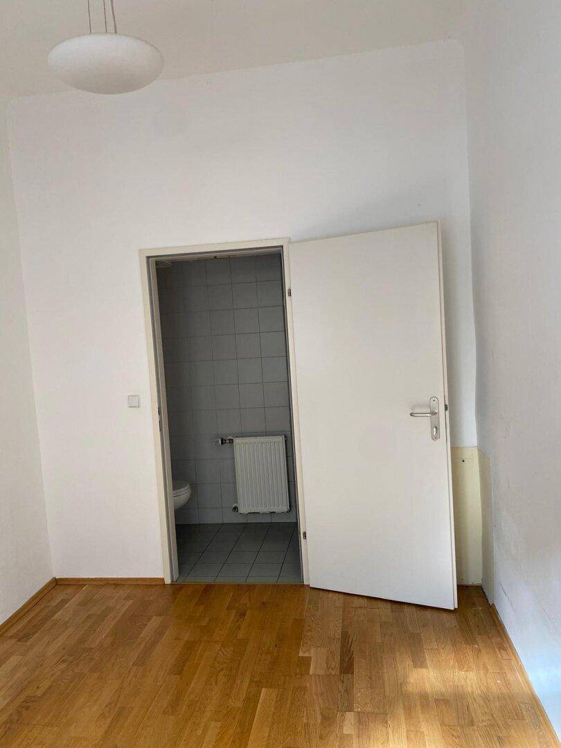 Schlafzimmer mit Holzparkettboden und einer Tür, die zu einem kleinen Badezimmer führt.