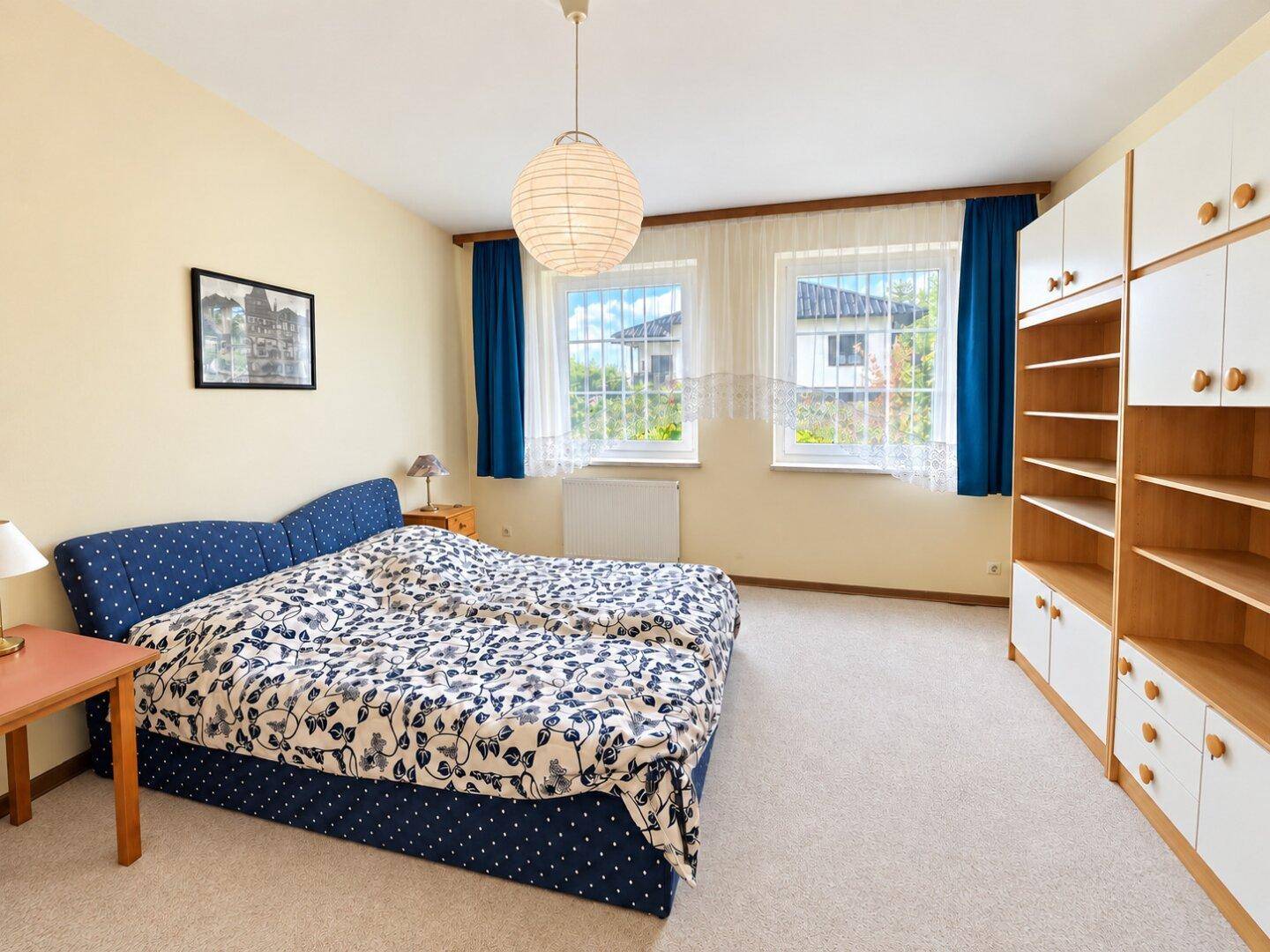 Helles Schlafzimmer mit Doppelbett, Teppichboden und Einbauschränken, mit Blick ins Grüne.