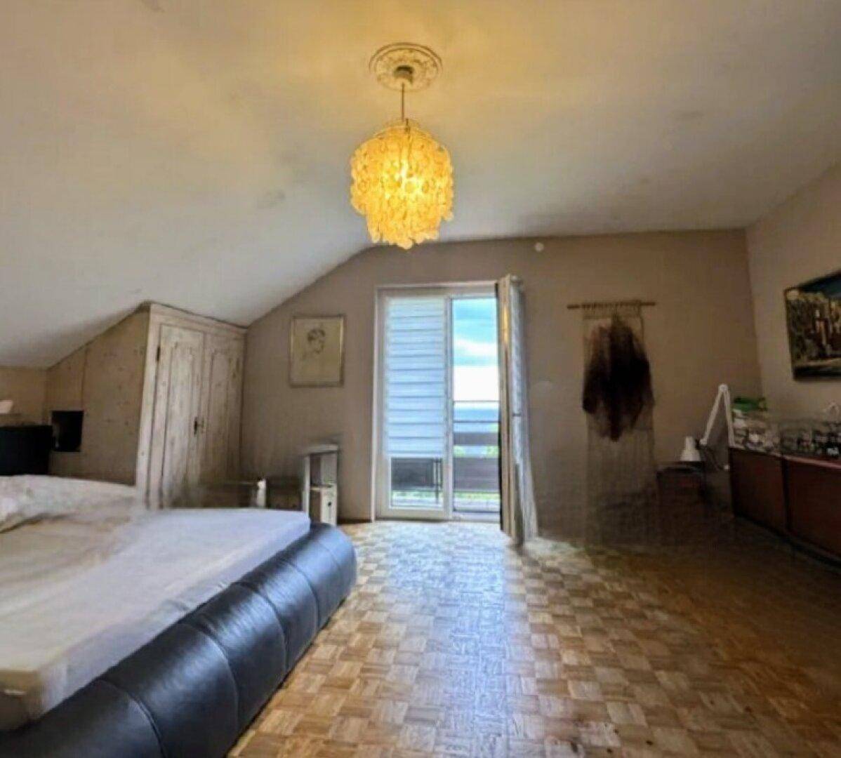 Helles Schlafzimmer im Dachgeschoss mit schräger Decke, Parkettboden und Zugang zu einem Balkon mit Fernblick.