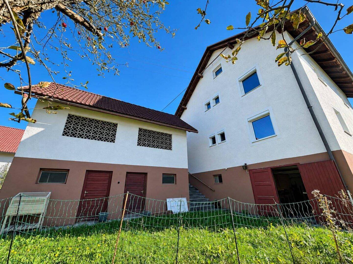 Zwei ländliche Gebäude mit weiß-brauner Fassade und roten Dächern, umgeben von Grünflächen.