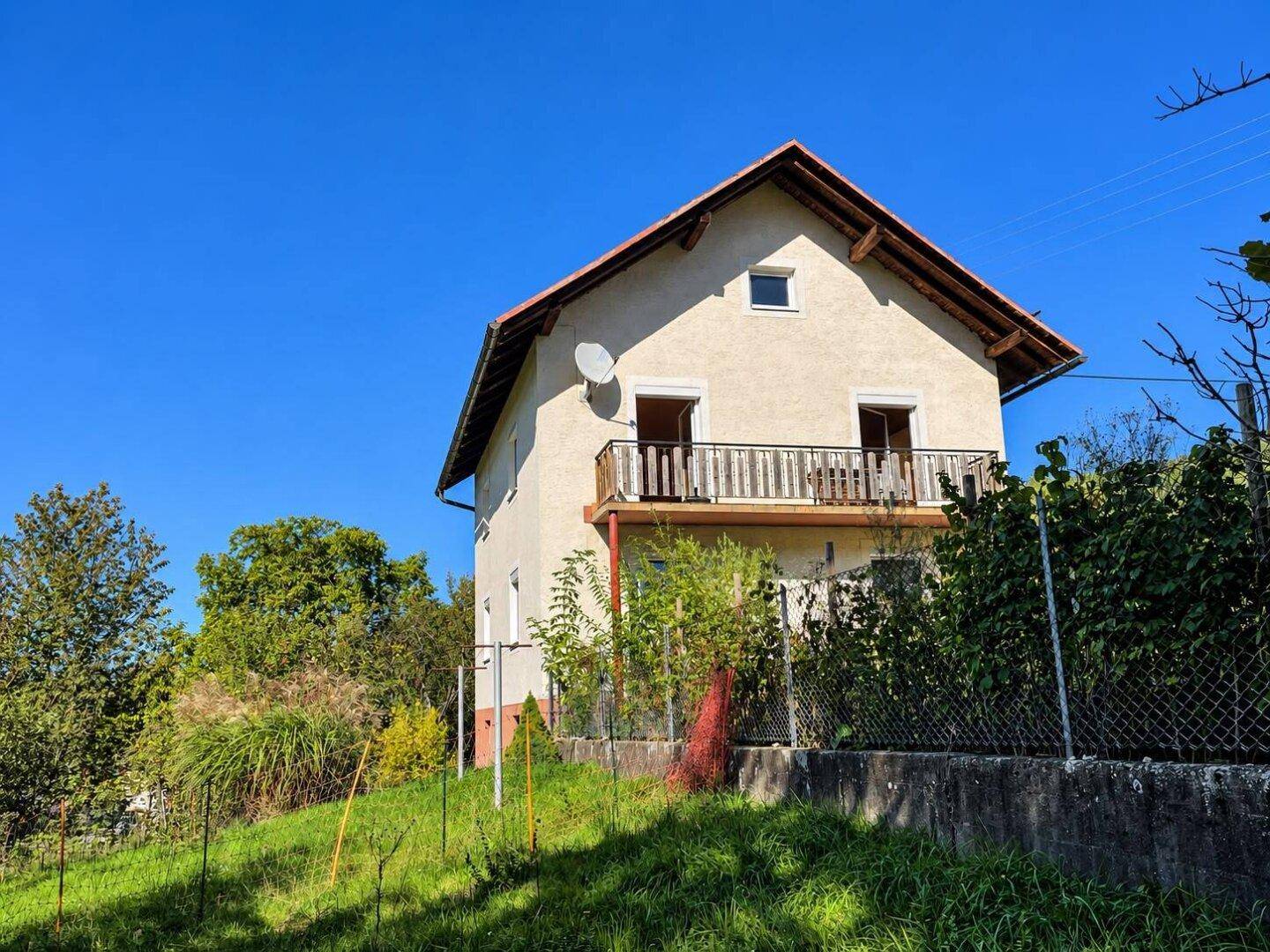 Ansicht des Hauses mit Balkon und Satellitenschüssel, umgeben von üppiger Vegetation.