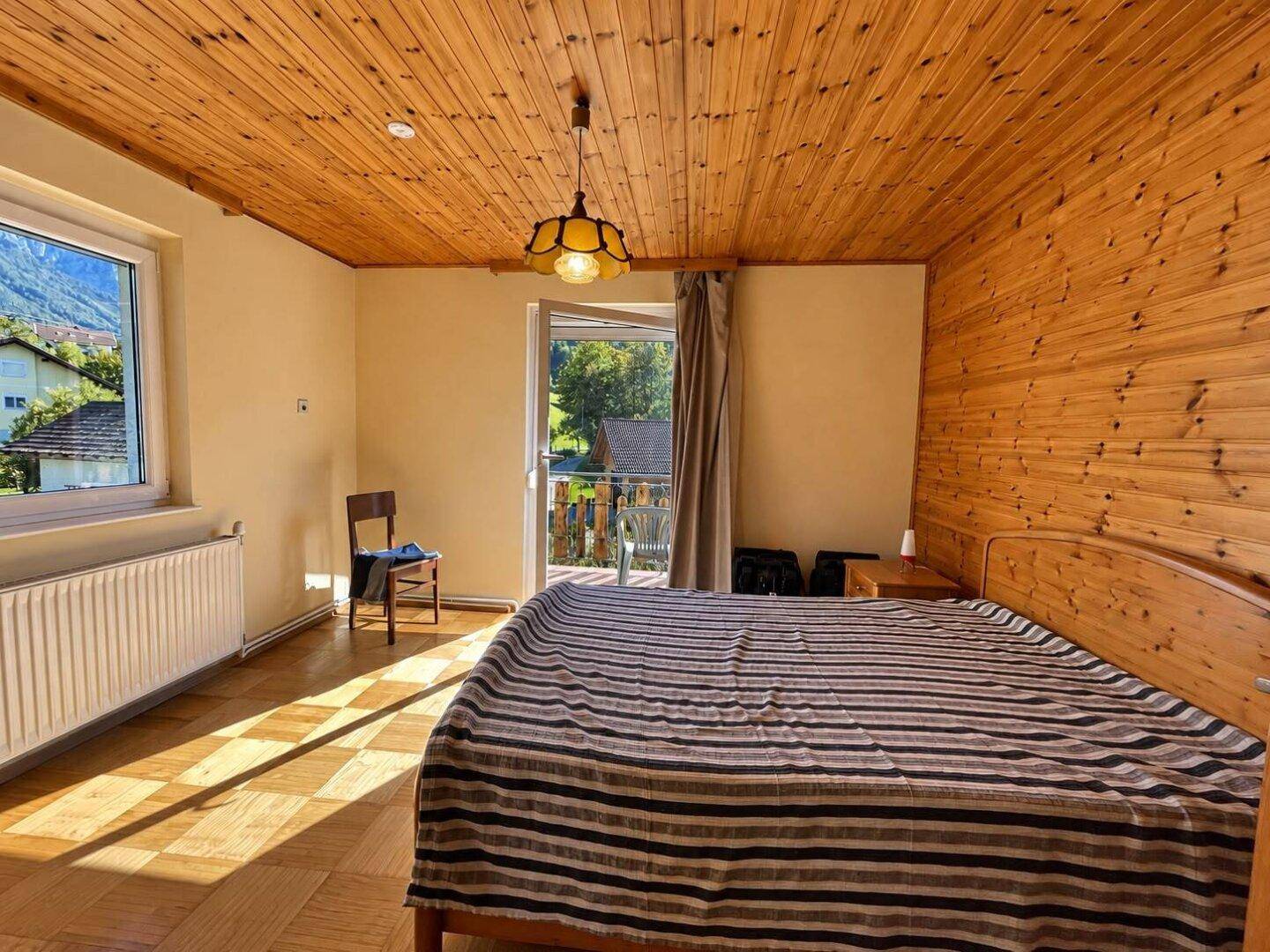 Schlafzimmer mit Holzdecke, Parkettboden und Balkonzugang, sonnendurchflutet.