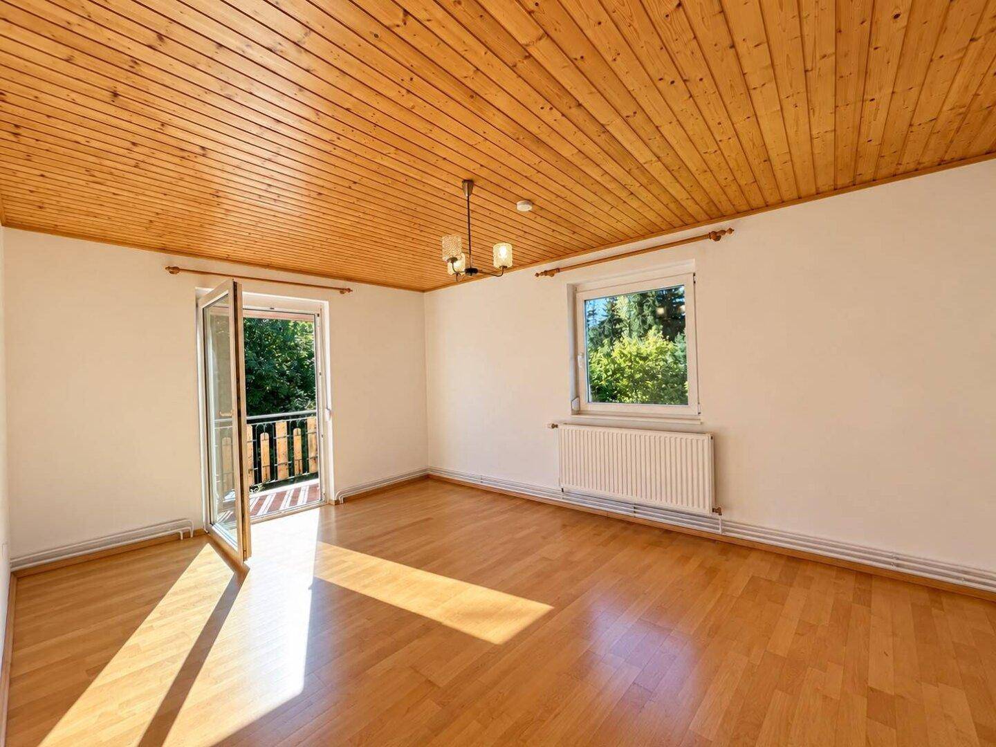 Helles Zimmer mit Holzdecke, Parkettboden und Zugang zu einem Balkon.
