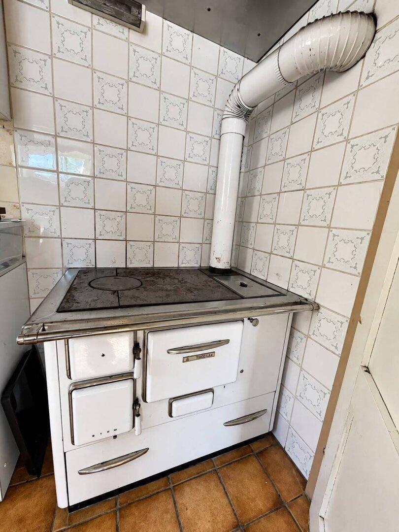 Alter Holzofen mit Kochplatte und Backfach in einer gefliesten Küchenecke.