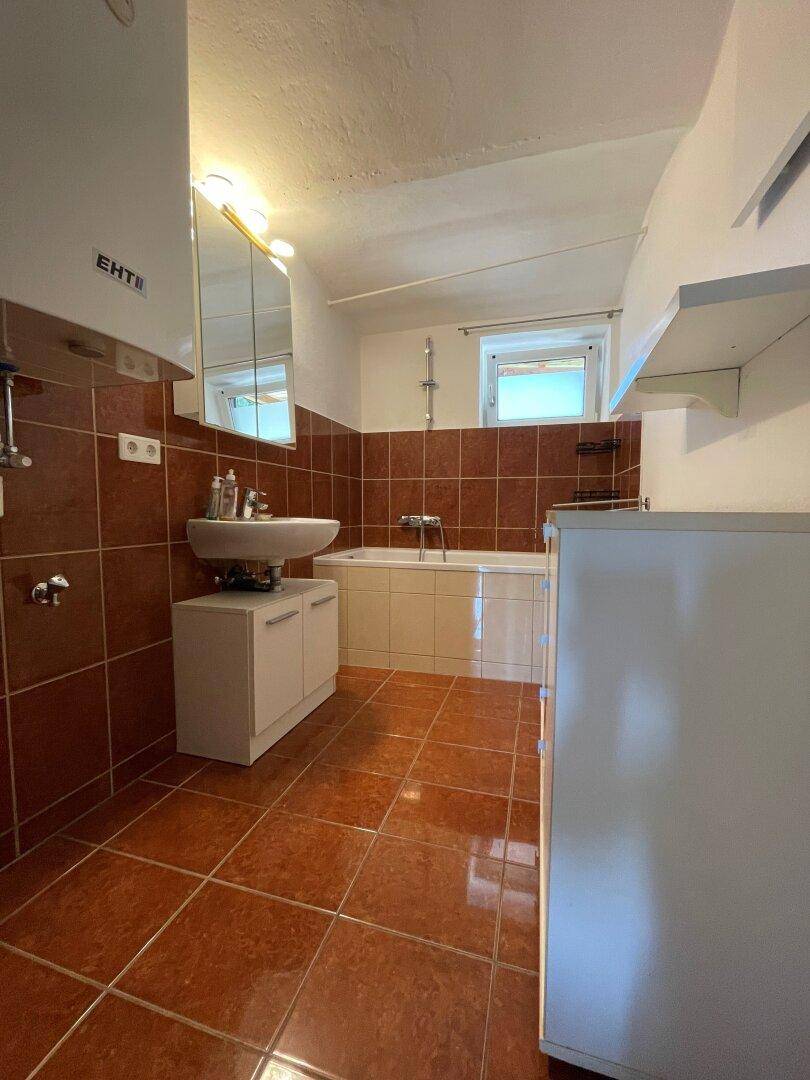 Badezimmer mit Terrakotta-Fliesenboden, Badewanne, Einzelwaschbecken und Fenster.