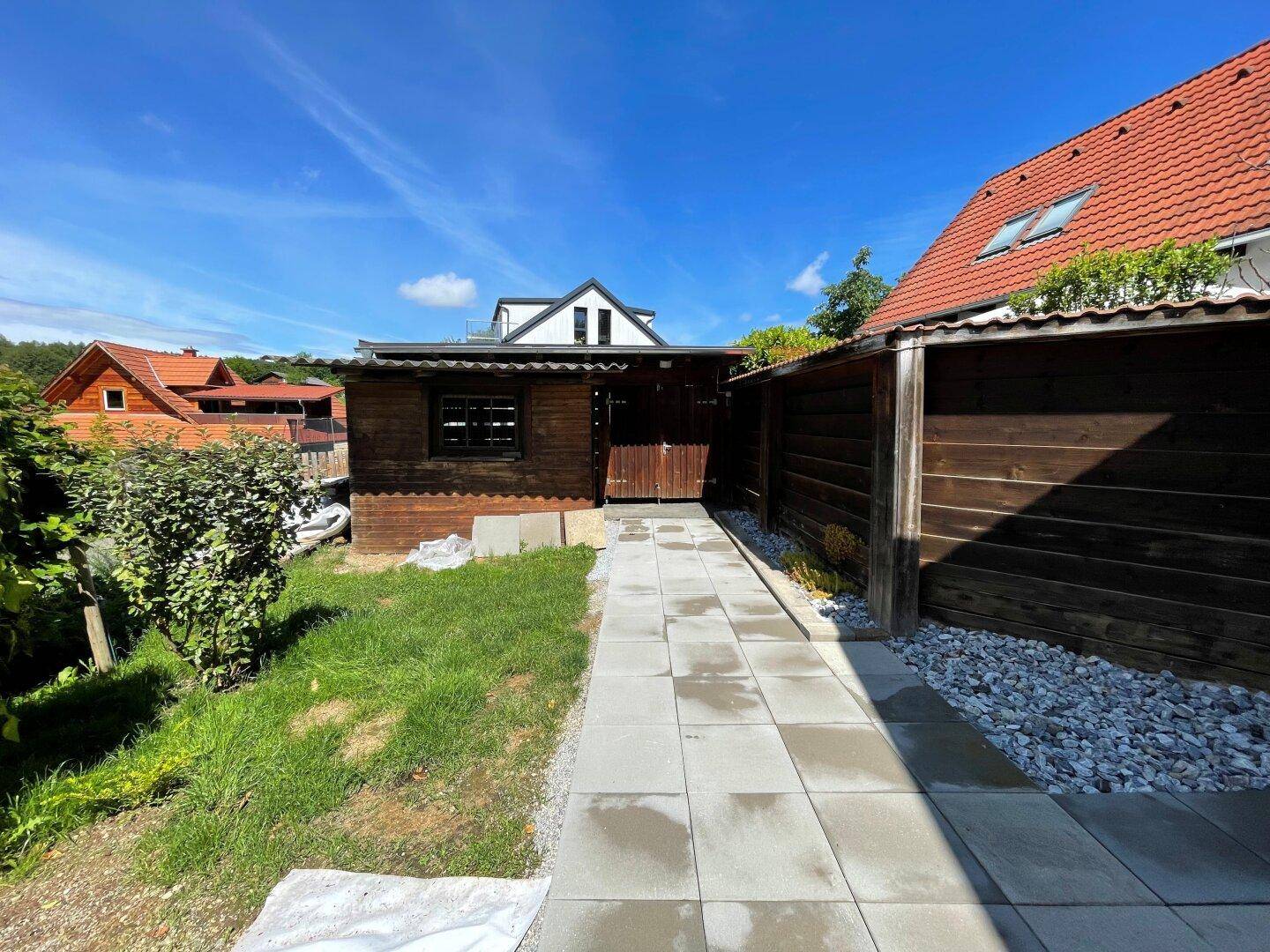 Gepflasterter Weg führt zu einem Holzgartenhaus, umgeben von Rasen und einem Holzzaun.