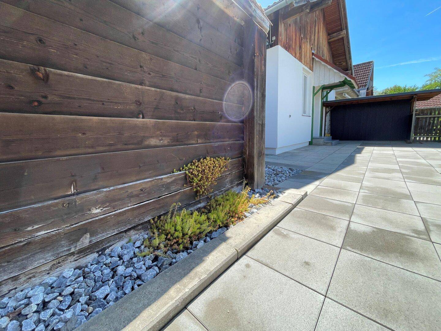 Detailansicht eines Holzzauns und Kiesbeets entlang eines gepflasterten Weges neben dem Haus.