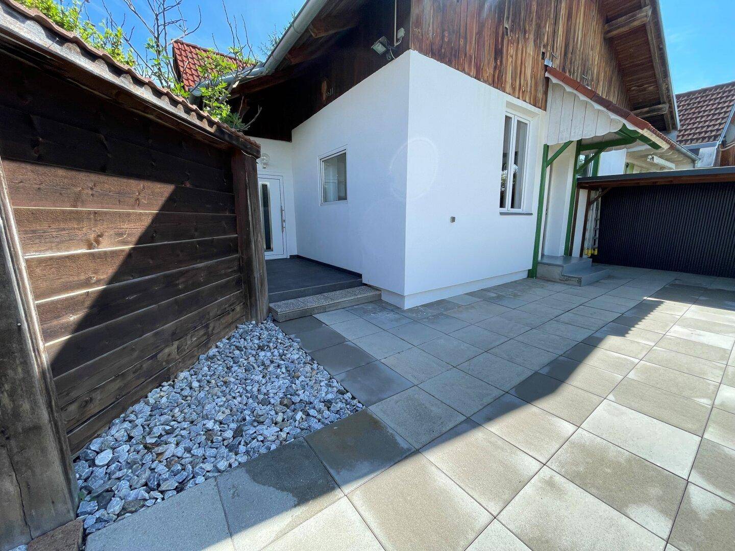 Außenansicht des Hauses mit frisch gestrichener weißer Fassade, Holzzaun und gepflastertem Eingangsbereich.