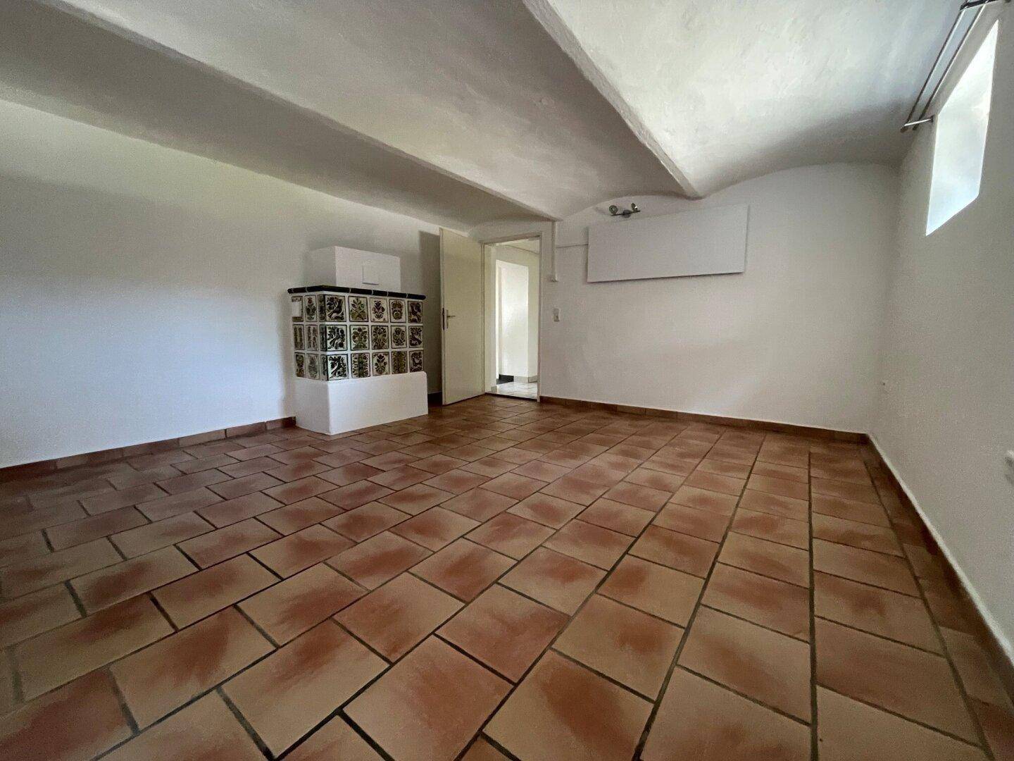Geräumiger Raum mit Terrakotta-Fliesenboden, traditionellem Kachelofen und gewölbter Decke.