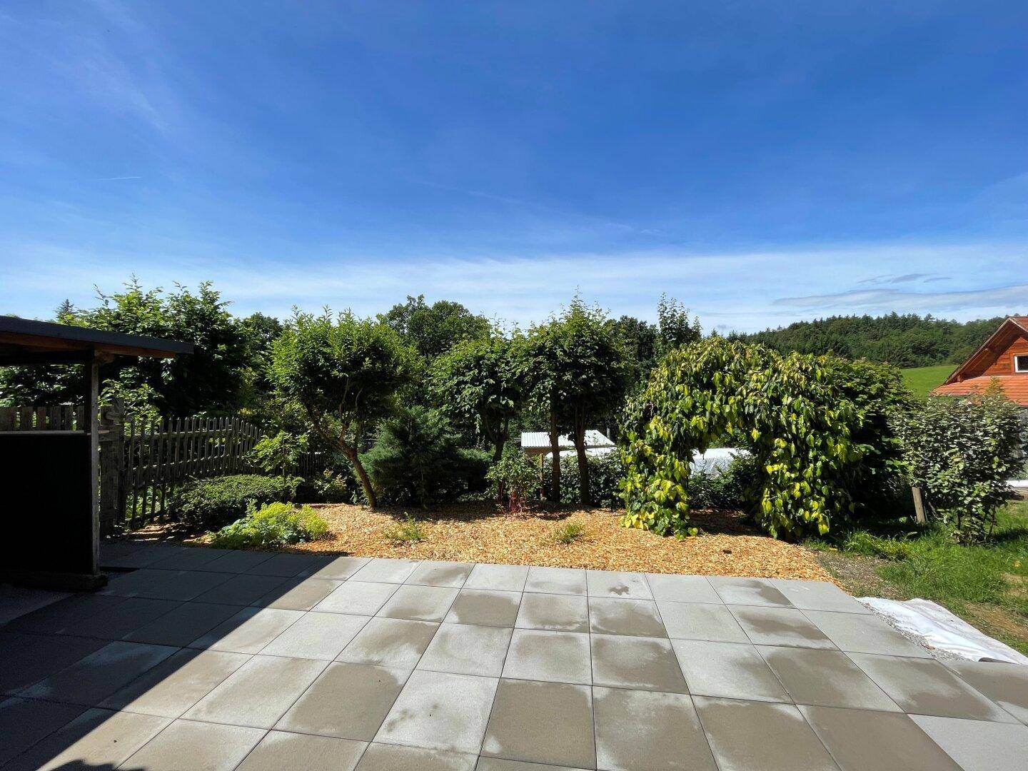 Weitläufige gepflasterte Terrasse mit Blick auf den gepflegten Garten und die grüne Landschaft.