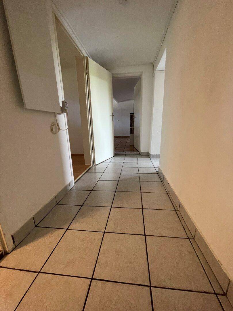 Heller Flur mit Fliesenboden und weißen Wänden, der zu den angrenzenden Räumen führt.